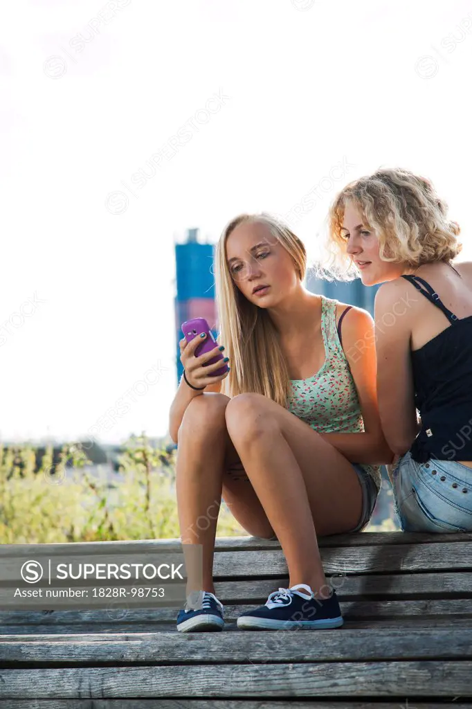 Teenage girls sitting on bench outdoors, looking at cell phone, Germany,08/21/2013