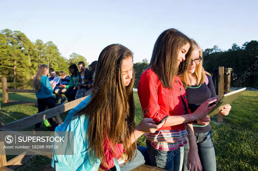 Group of pre-teens sitting on fence, looking at tablet computers and cellphones, outdoors, Florida, USA. 10/22/2012