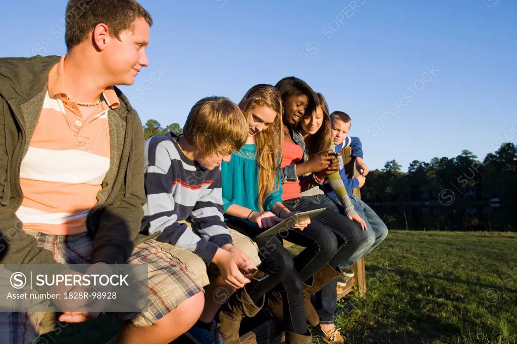 Group of pre-teens sitting on fence, looking at tablet computer and cellphones, outdoors, Florida, USA. 10/22/2012