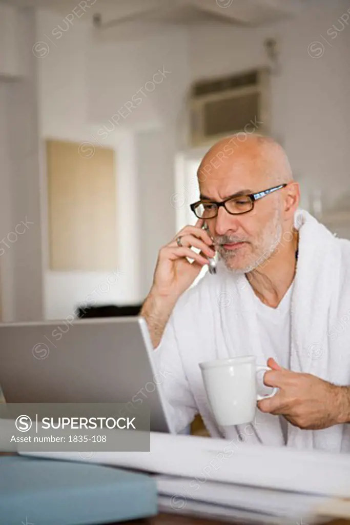 Mature man holding a cup of coffee and looking at a laptop