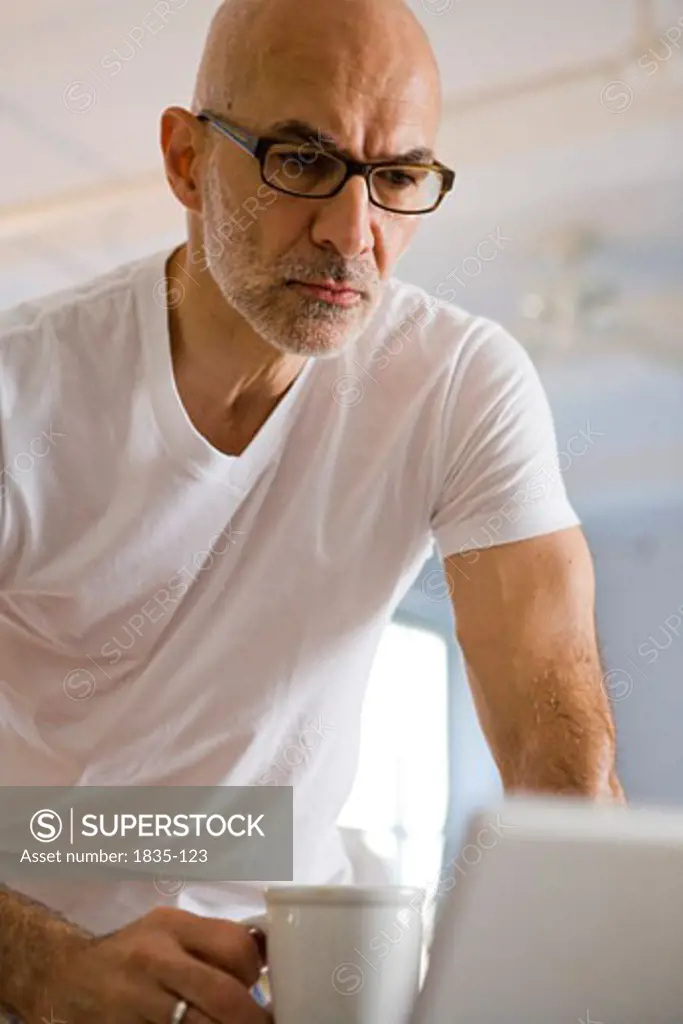 Mature man holding a cup of coffee and looking at a laptop