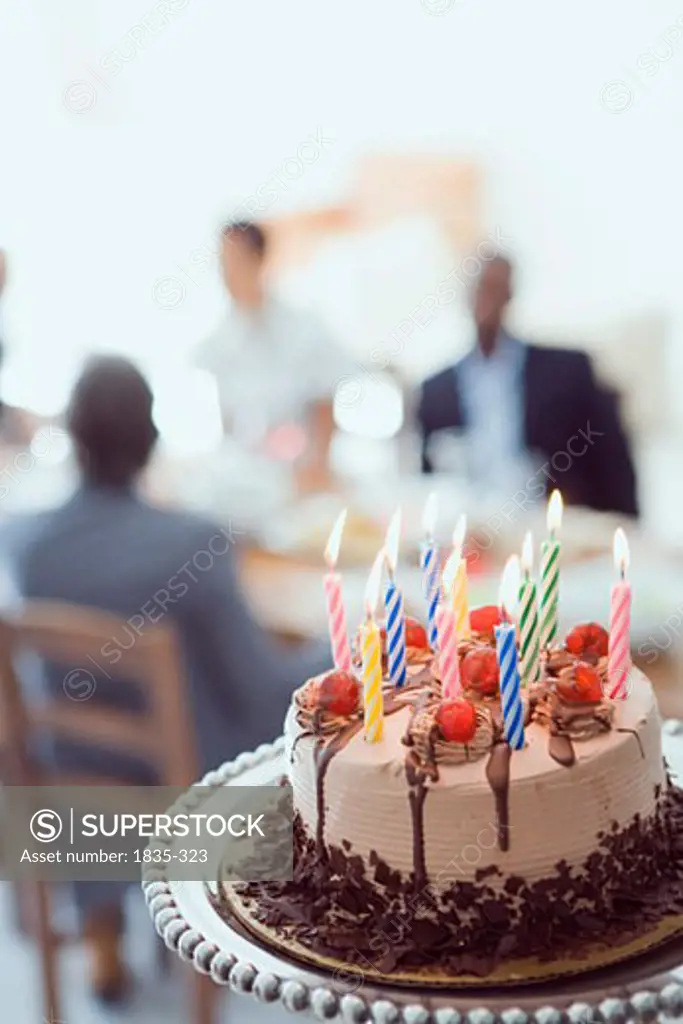 Close-up of a birthday cake with three people sitting at the dining table in the background