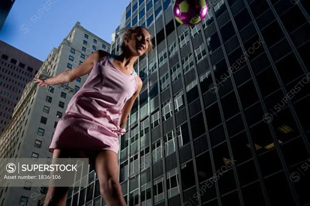 Low angle view of a young woman heading a soccer ball with buildings in the background