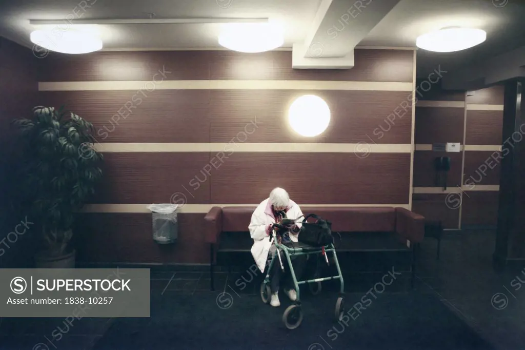 Eldery Woman With Walker Sitting in Building Lobby