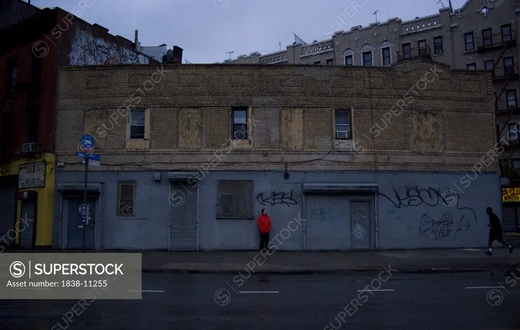 Young Man in Red Coat Waiting Against Rundown Building, Brooklyn, New York, USA