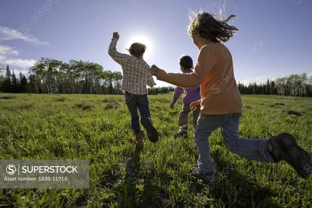 Three Young Girls Running in Grass Field, Rear View, Oak Creek, Colorado, USA