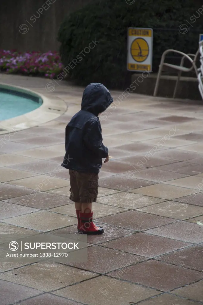 Young Boy Standing Near Pool in the Rain