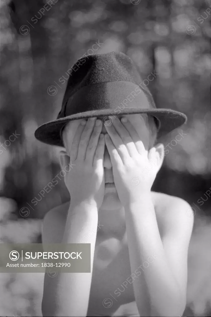 Young Boy Wearing Fedora Hat and Covering Face With Hands
