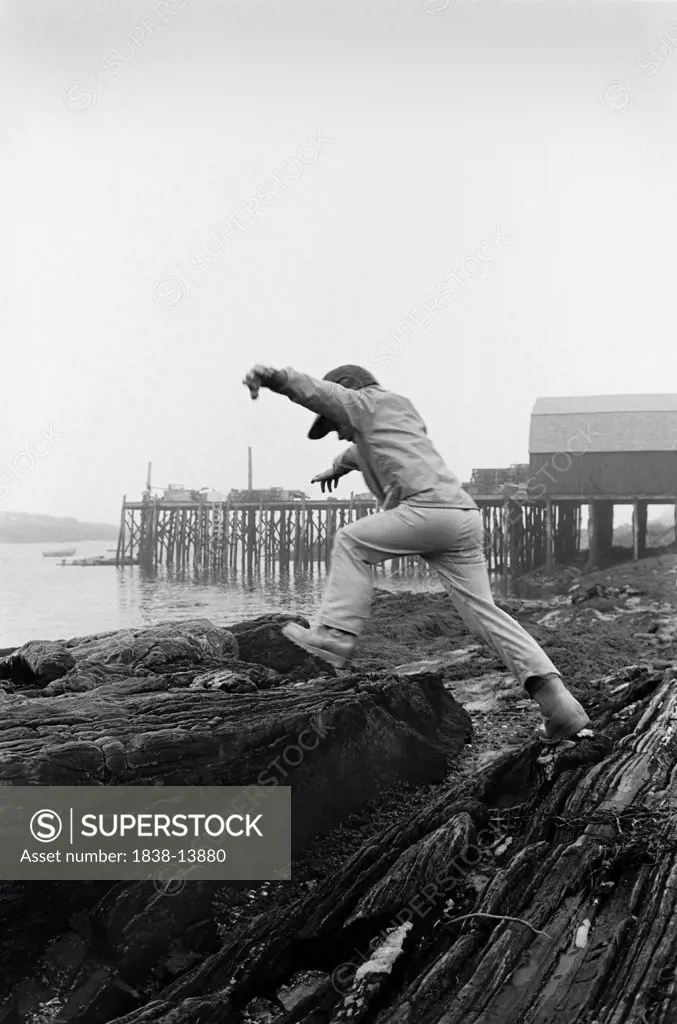 Boy Jumping on Rocks Along Shore, Rear View