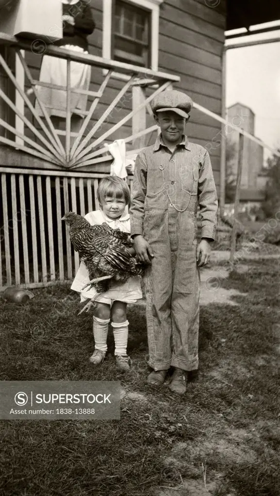 Young Boy Standing Next to Young Girl Holding Chicken
