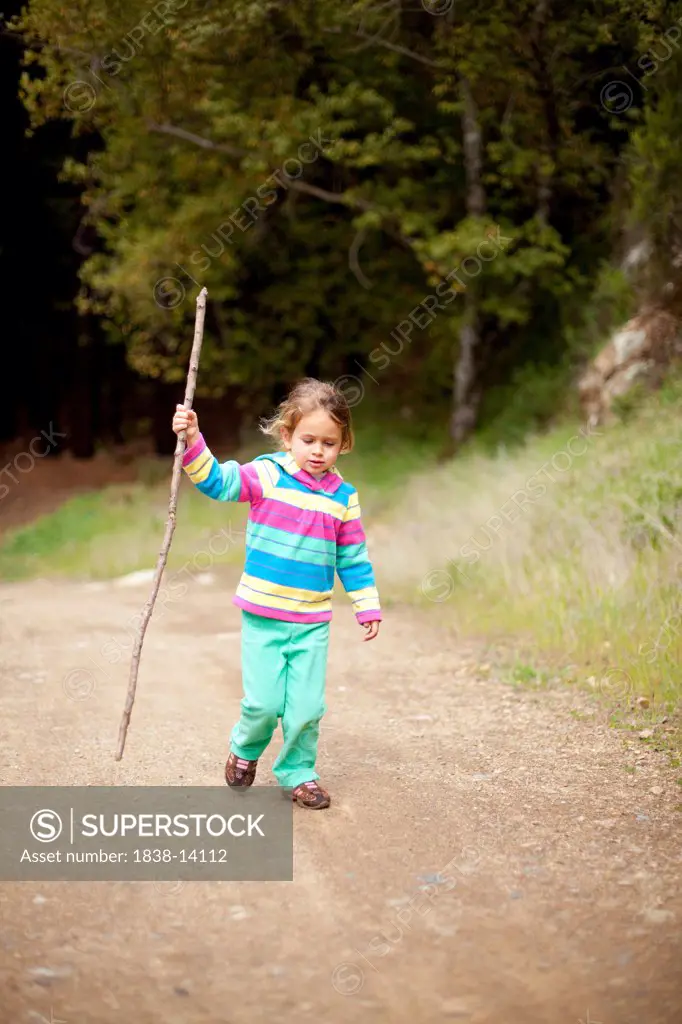 Young Girl Walking Along Dirt Road With Walking Stick
