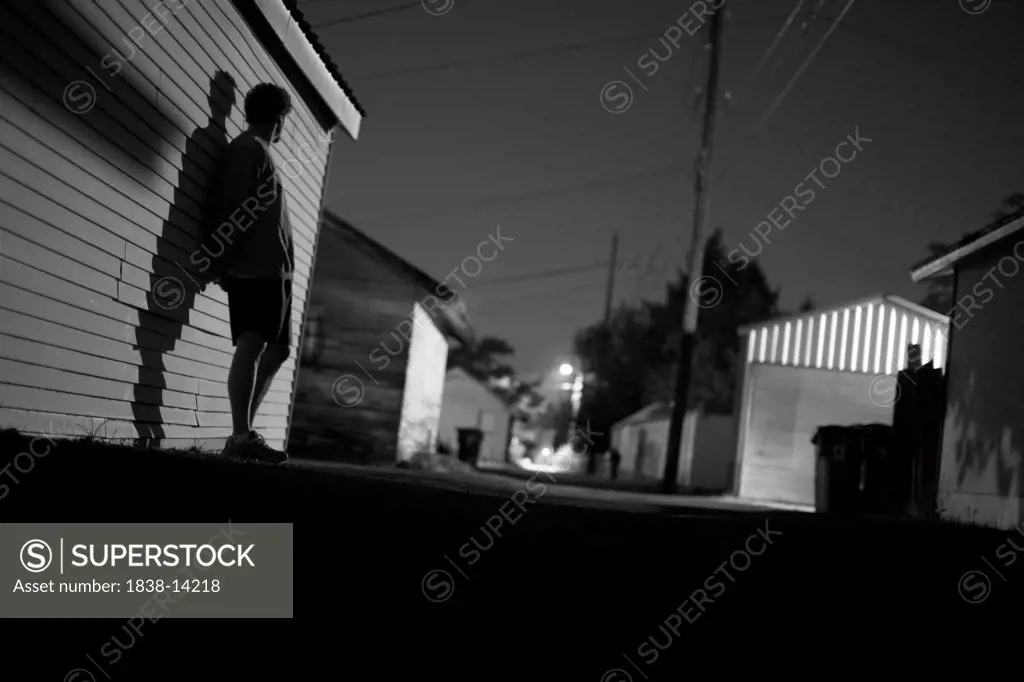 Young Man Leaning Against Side of Building at Night