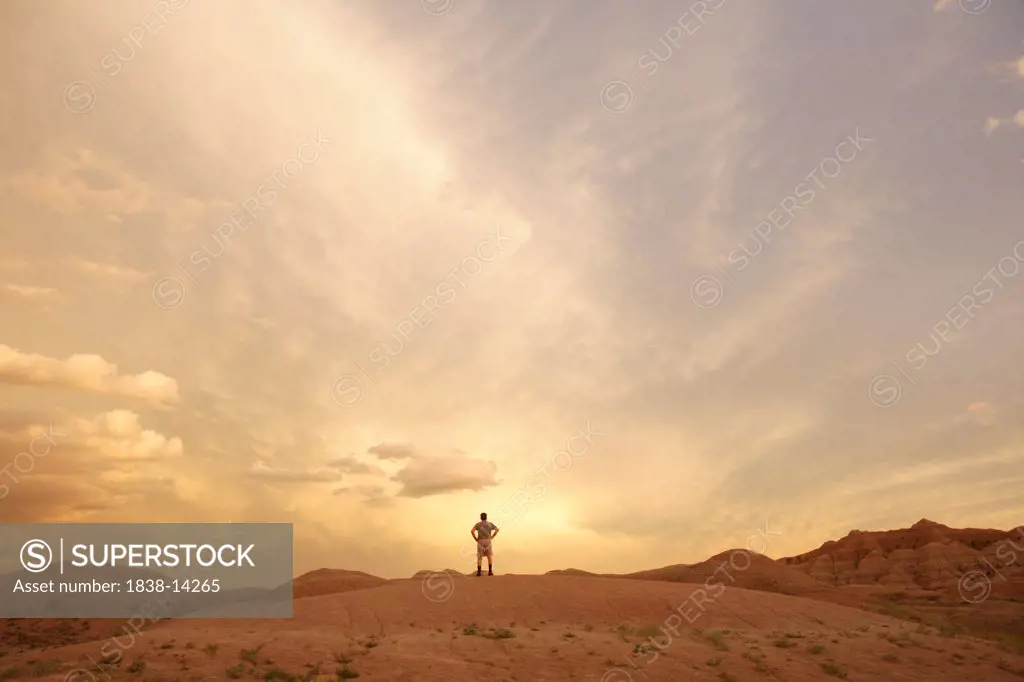 Man Standing on Small Hill While Looking at Vista at Sunset, Badlands National Park, South Dakota, USA