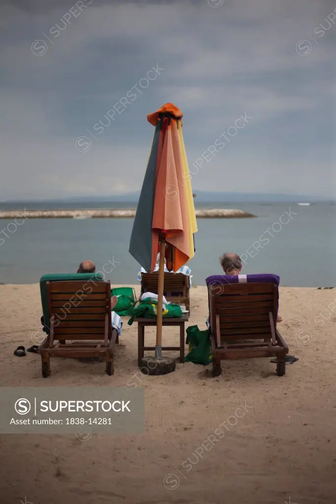 Two Men Relaxing on Lounge Chairs on Beach, Rear View, Bali, Indonesia