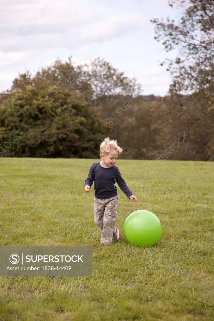 Young Boy Playing With Large Green Ball in Field