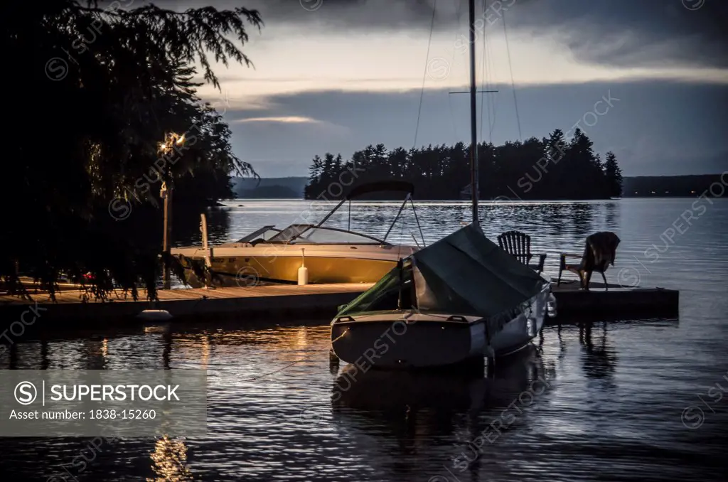 Speedboat and Sailboat Parked Against Dock in Lake at Dusk