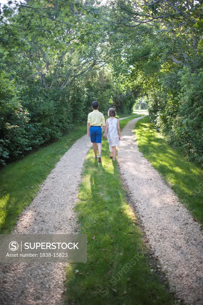 Young Boy and Girl Holding Hands While Walking Down Rural Driveway, Rear View