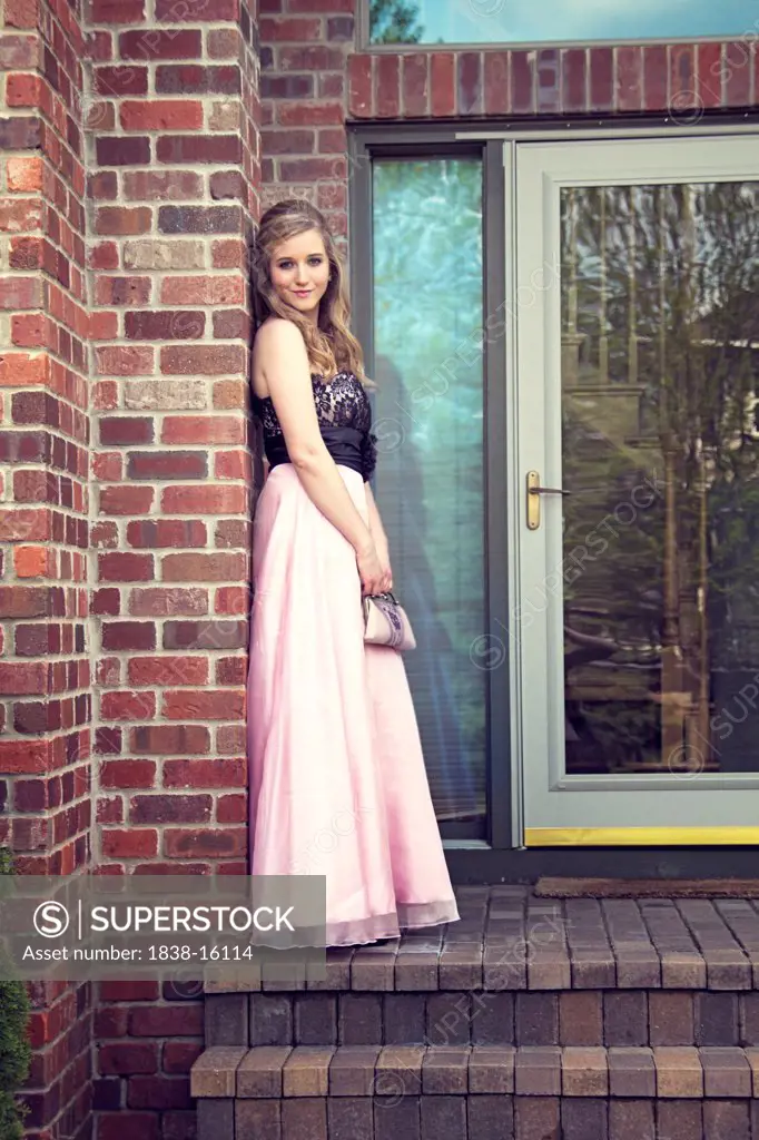 Smiling Young Woman Wearing Strapless Gown Leaning Against Brick Wall, Portrait