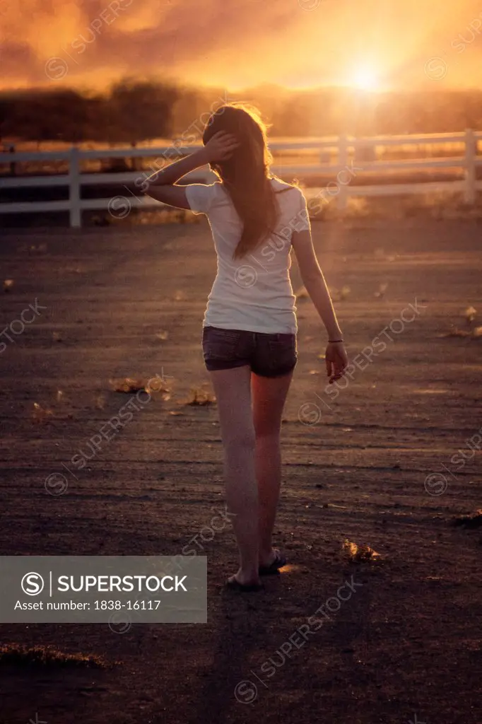 Teen Girl in Shorts and T-Shirt Walking Towards Sunset, Rear View
