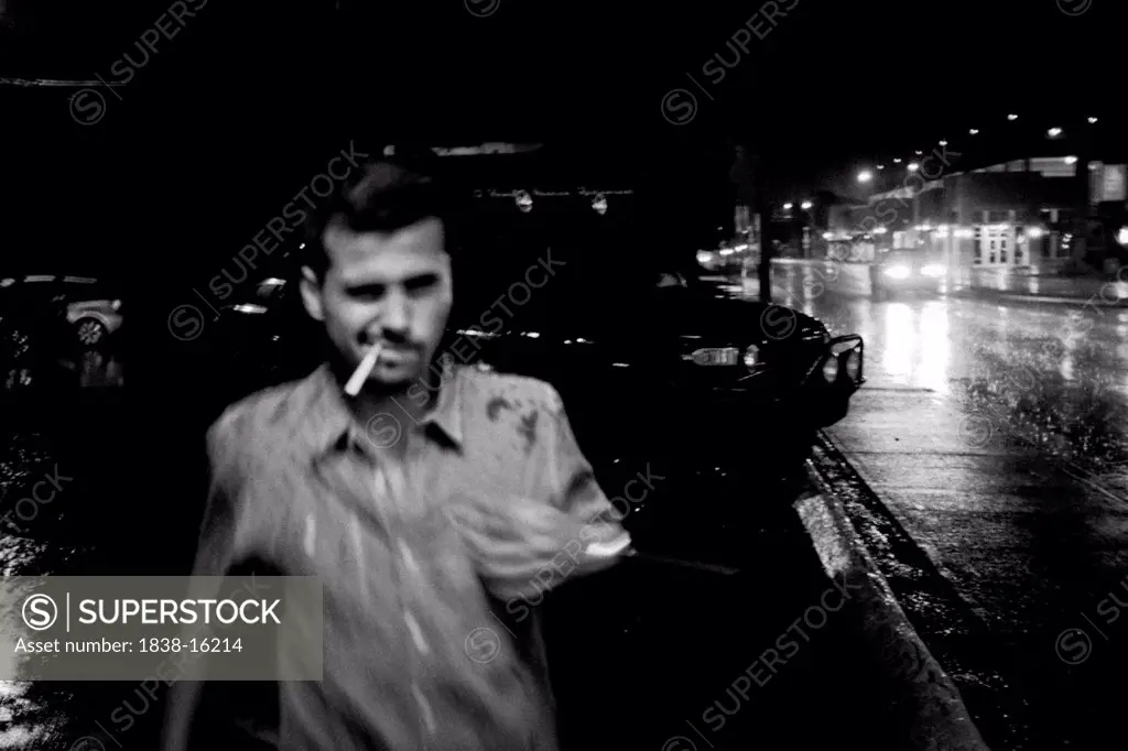 Man With Cigarette in Mouth Walking in Rain at Night