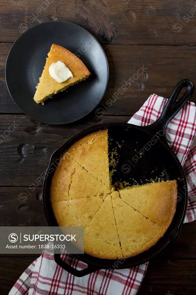 Cornbread in Cast-iron Skillet and Slice of Cornbread with Butter on Small Plate, High Angle View