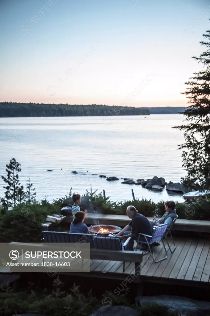 Family Gathered Around Fire Pit Near Lake at Dusk