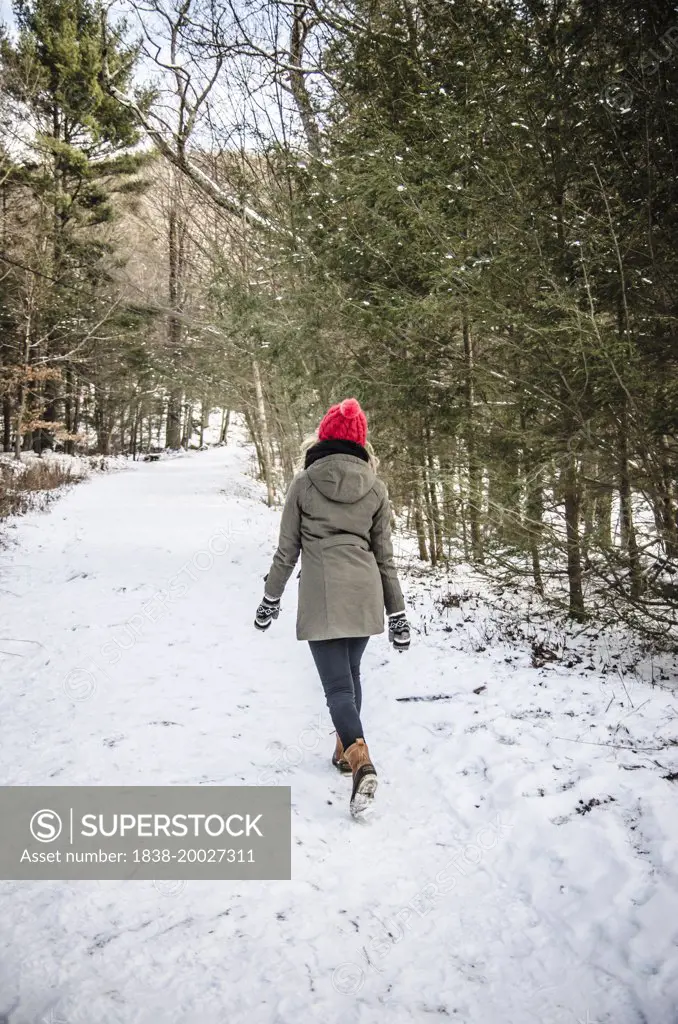 Young Woman in Winter Clothes Leisurely Walking Along Snow-Covered Path Through Trees