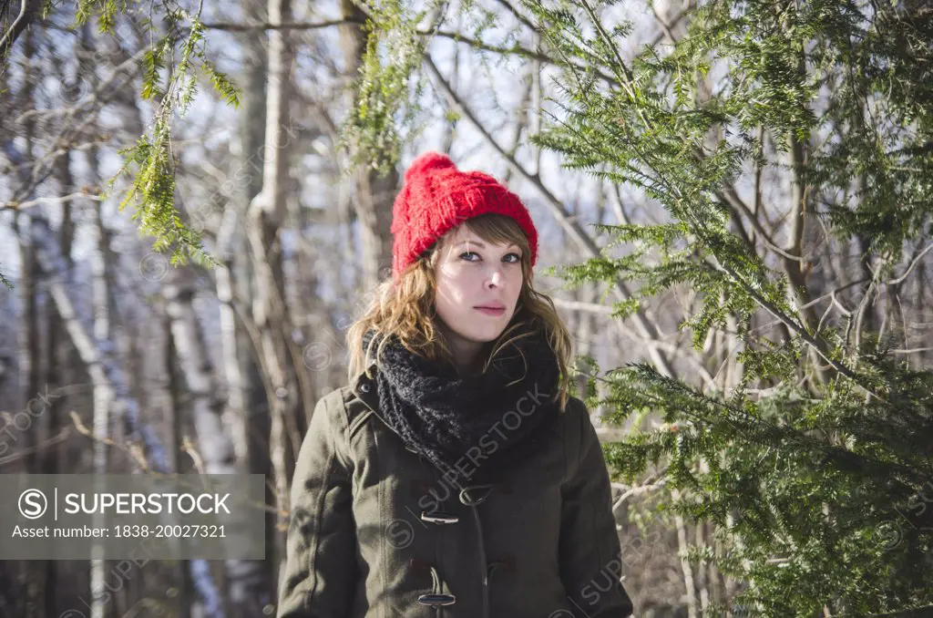 Stoic Young Woman in Winter Clothes Standing Among Tree Branches