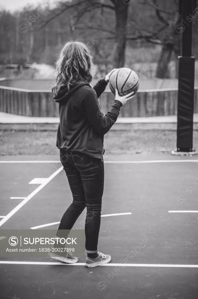 Young Woman in Jeans and Hooded Sweatshirt Holding Basketball