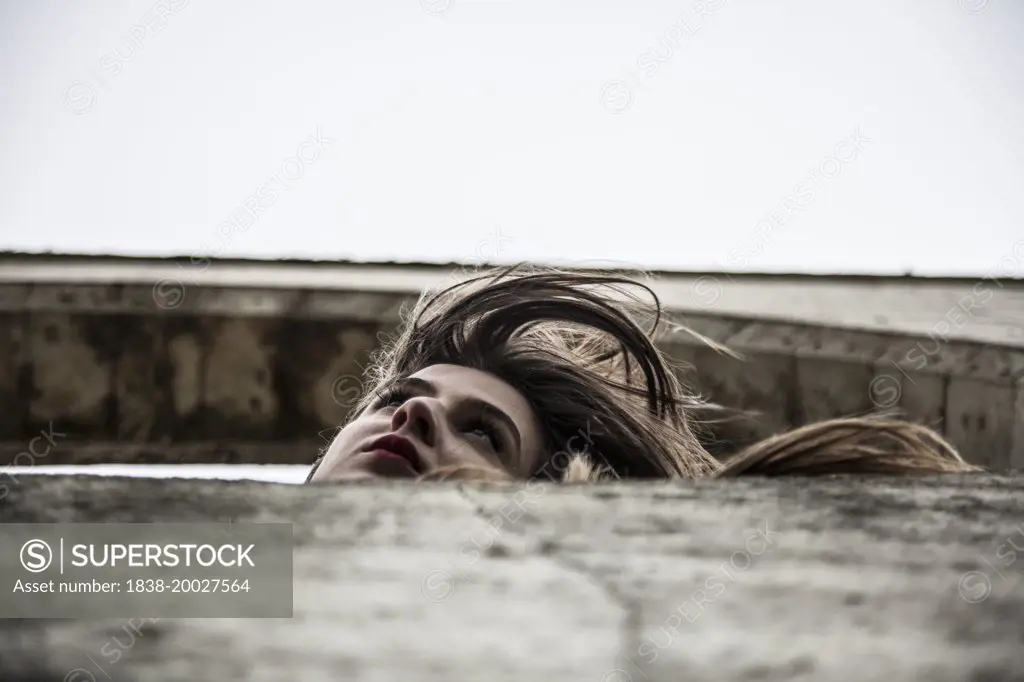 Contemplative Young Woman Leaning out of Arched Structure Outdoor, Low Angle View