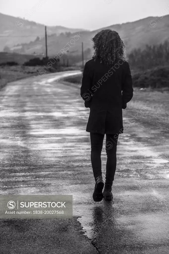 Young Man with Curly Hair Walking Down Road, Rear View