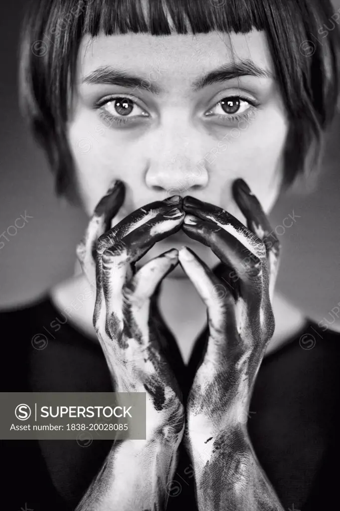 Portrait of Young Woman with Black Paint on Hands Covering Mouth
