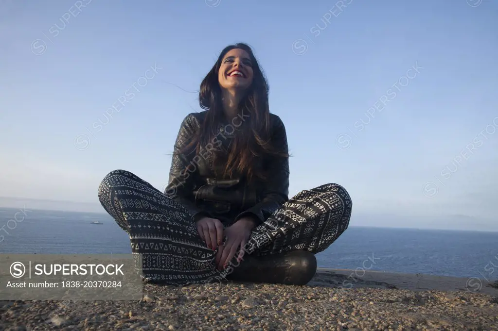 Smiling Woman Sitting on Sea Cliff