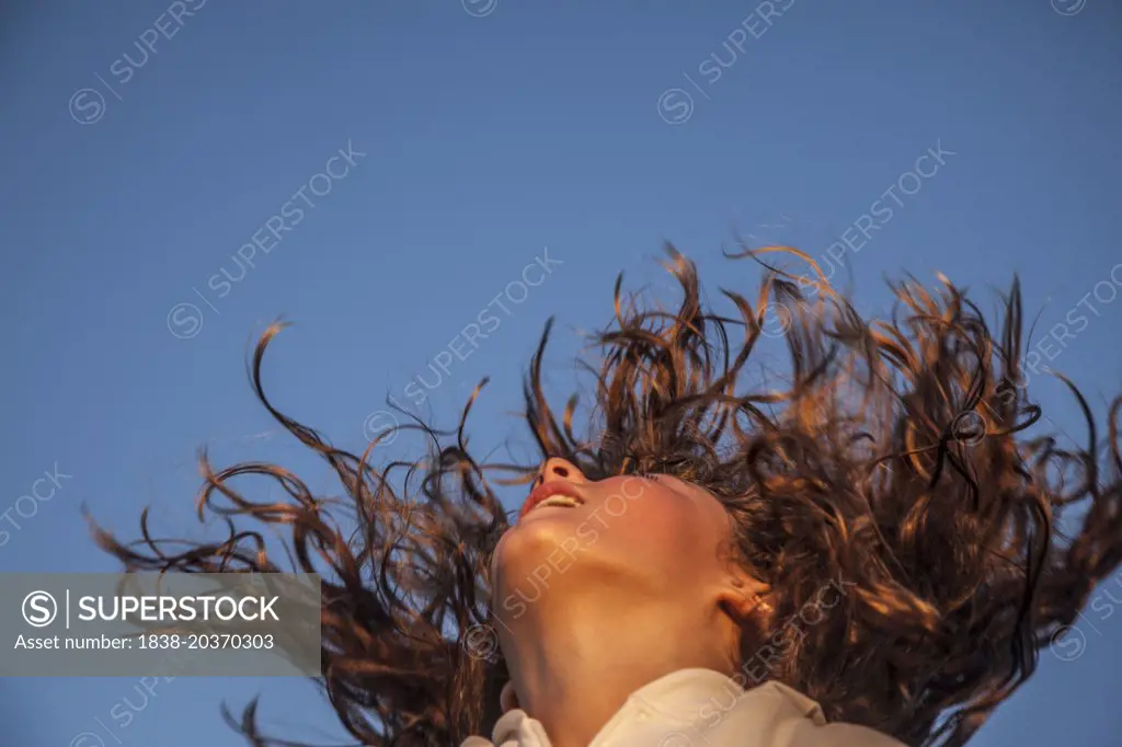 Young Girl Shaking Long Curly Hair Against Blue Sky, Low Angle View