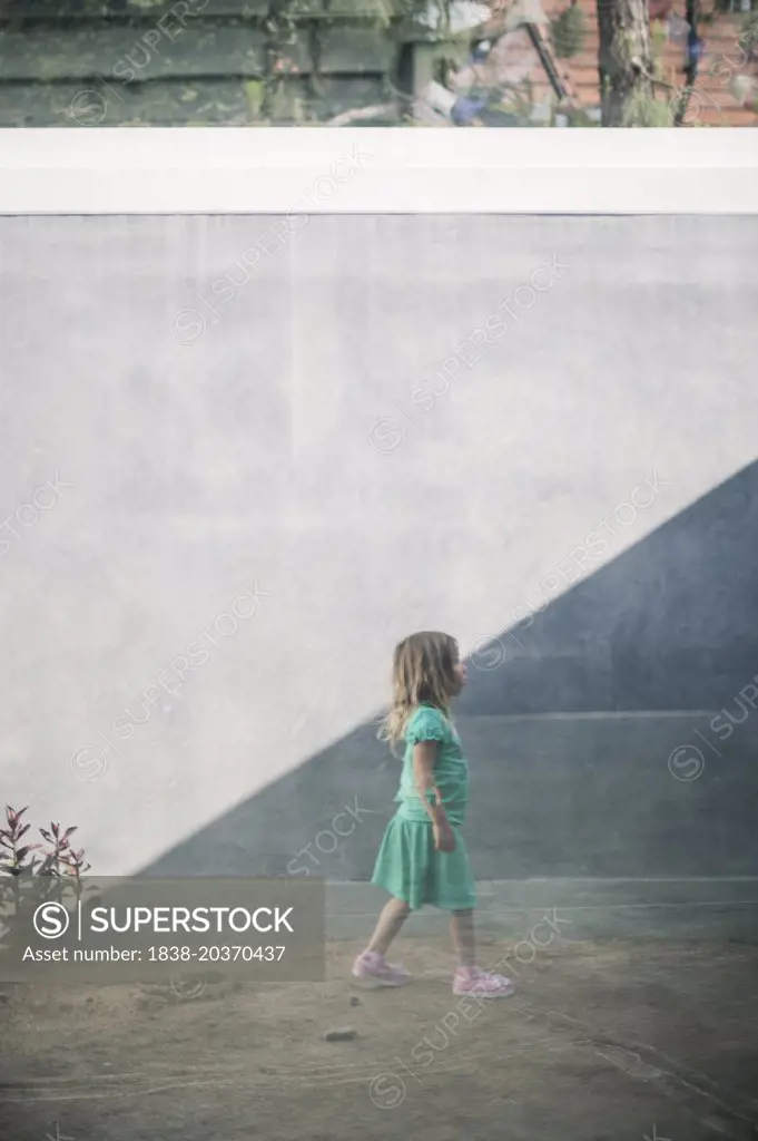 Young Girl Walking in Dirt Against Gray Wall