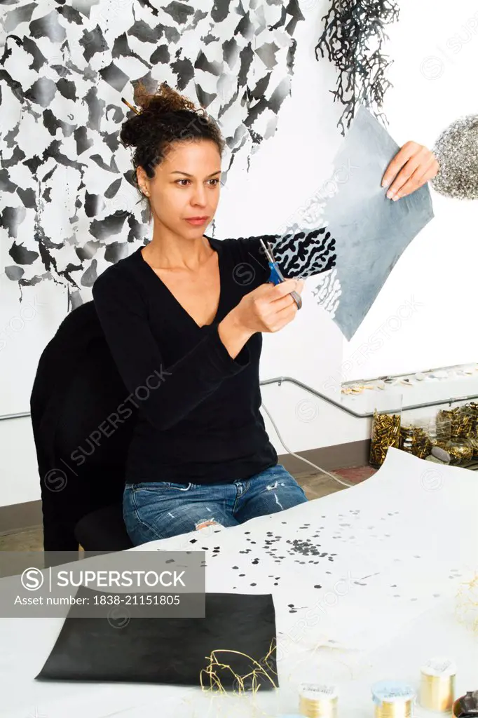 Dark Haired Woman Using Scissors and Grey Paper in Artist's Studio