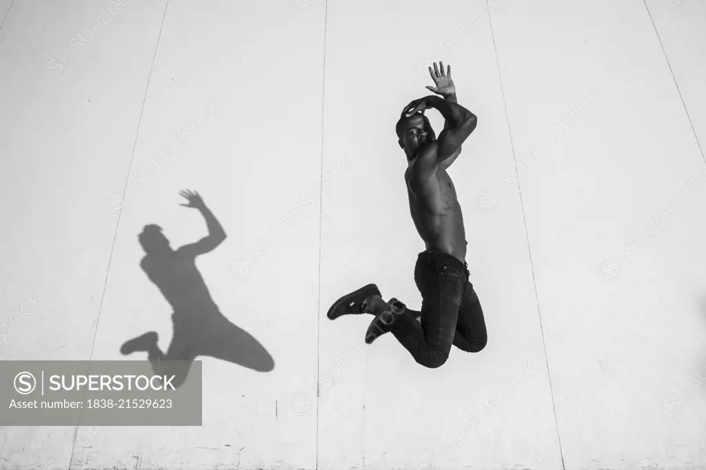 Portrait of Shirtless Young Adult Man Jumping with Shadow Cast Against Wall