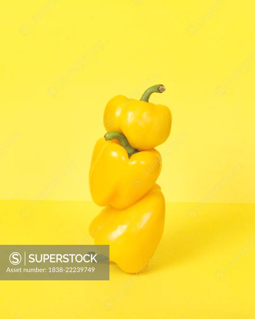 Three Stacked Yellow Peppers against Yellow Background