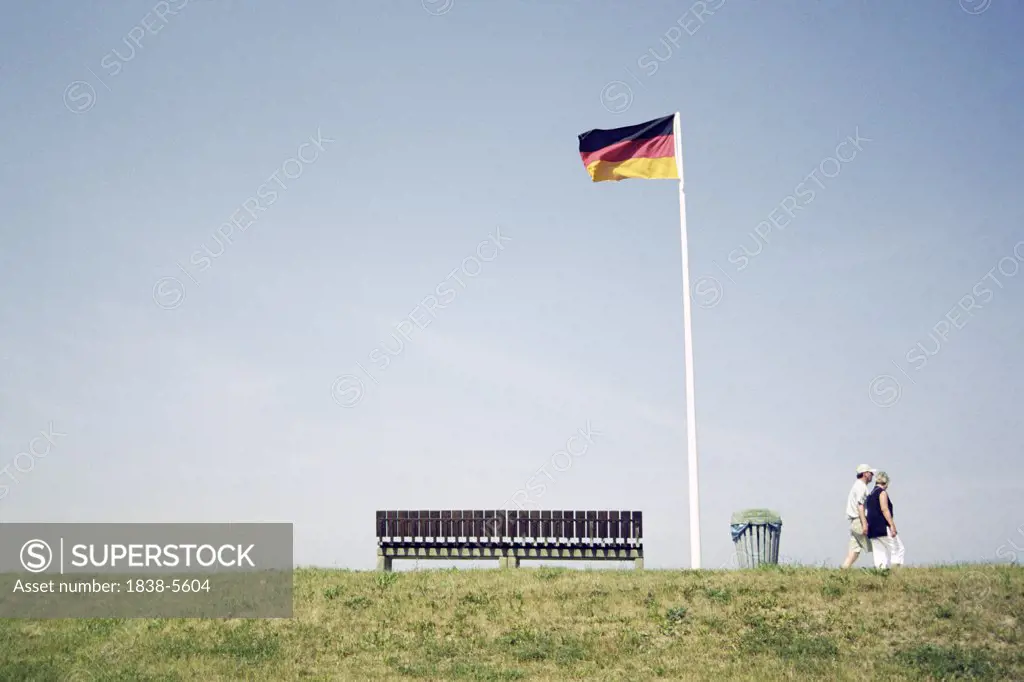 Couple walking along dike with German flag next to a bench, Schonberg, Schleswig-Holstein, Germany