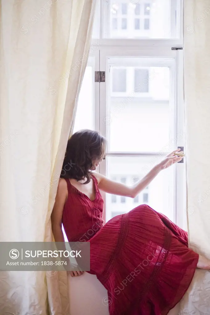 Young woman sitting on sill while looking through window