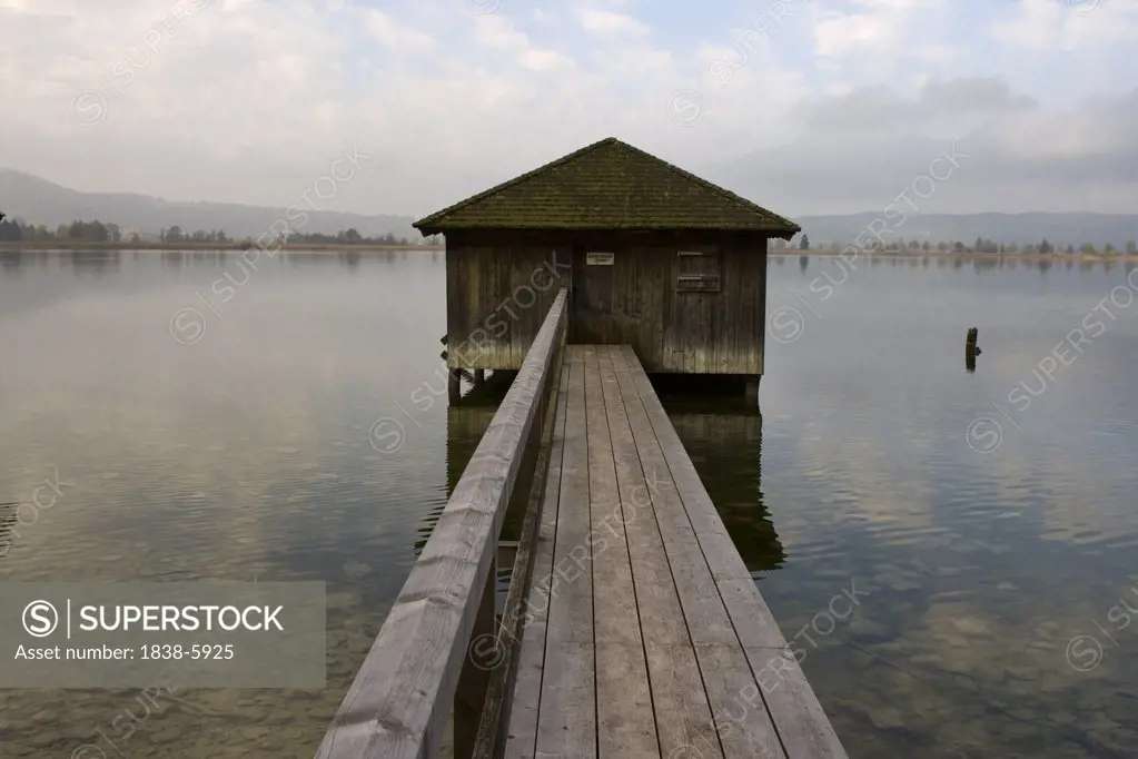 View along a jetty to a boathouse in a lake