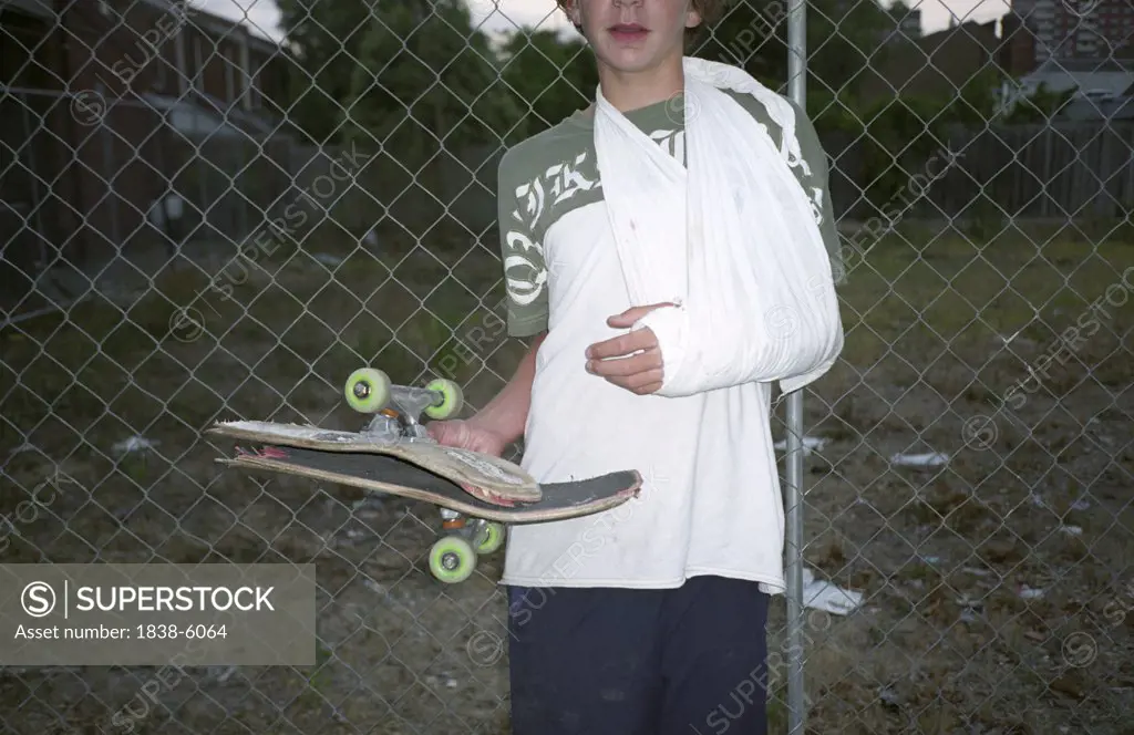 Boy with sling on arm holding broken skateboard, Melbourne, Victoria, Australia