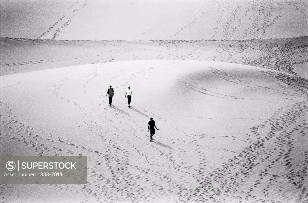 Aerial View of Three Figures Walking Across Sand Dune