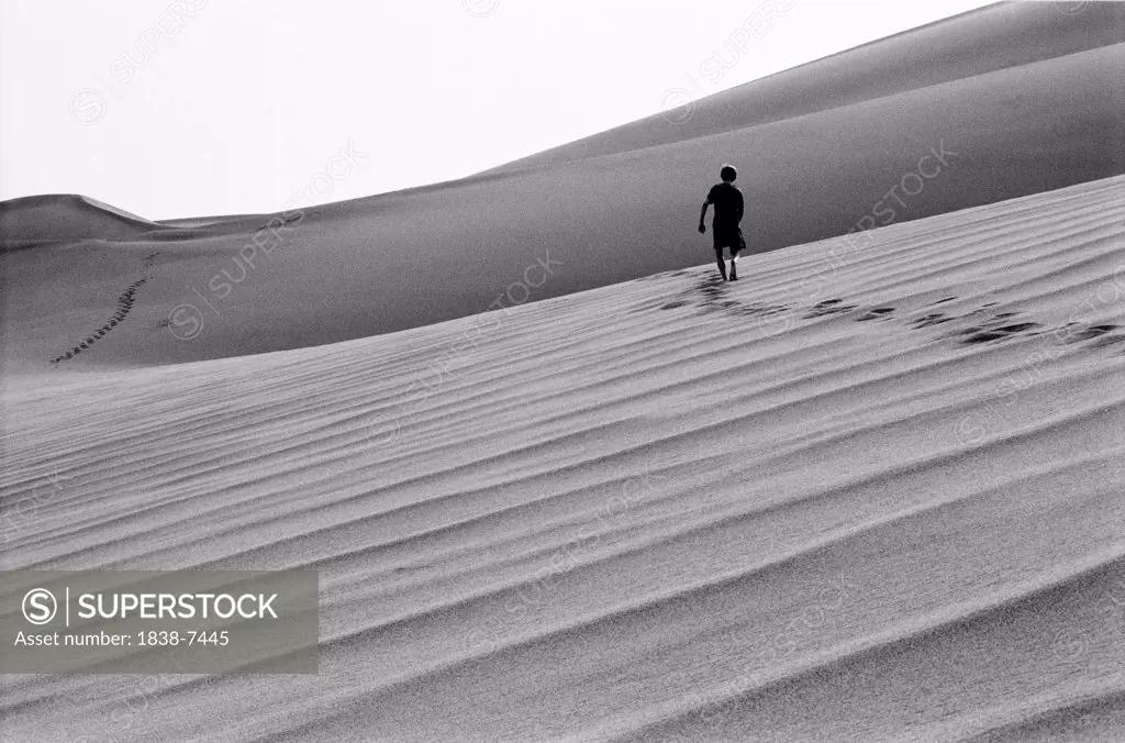 Silhouetted Boy Walking Across Sand Dune