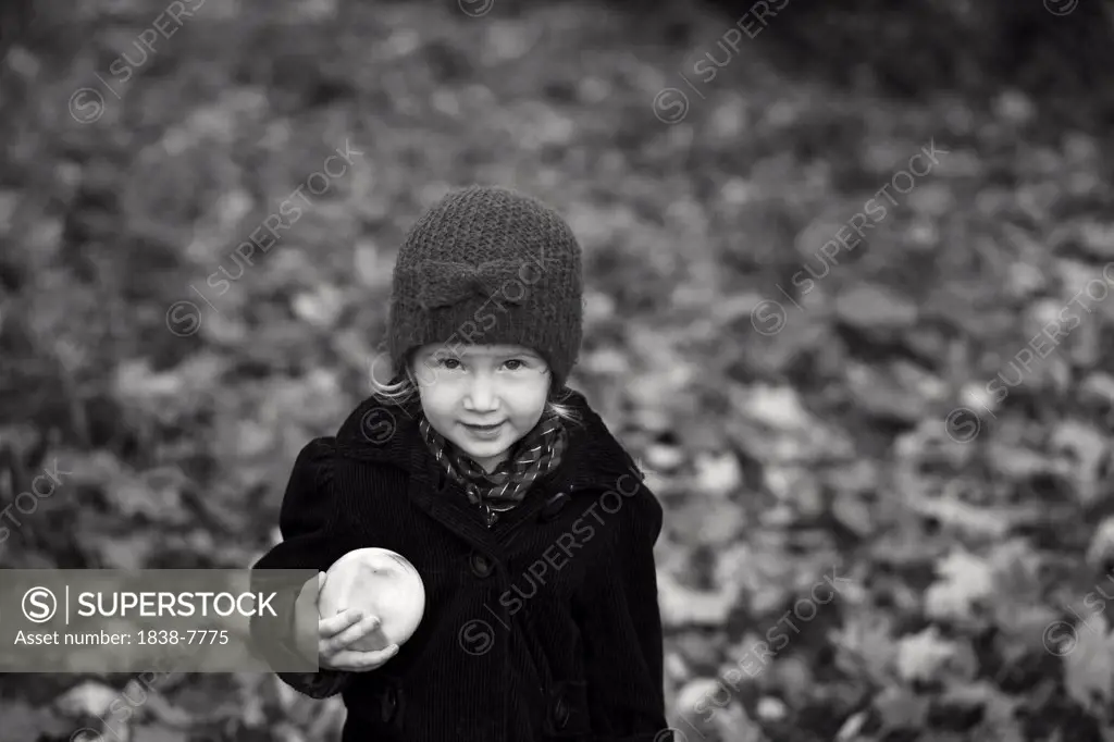 Young Blonde Girl in Winter Coat and Hat Holding Apple