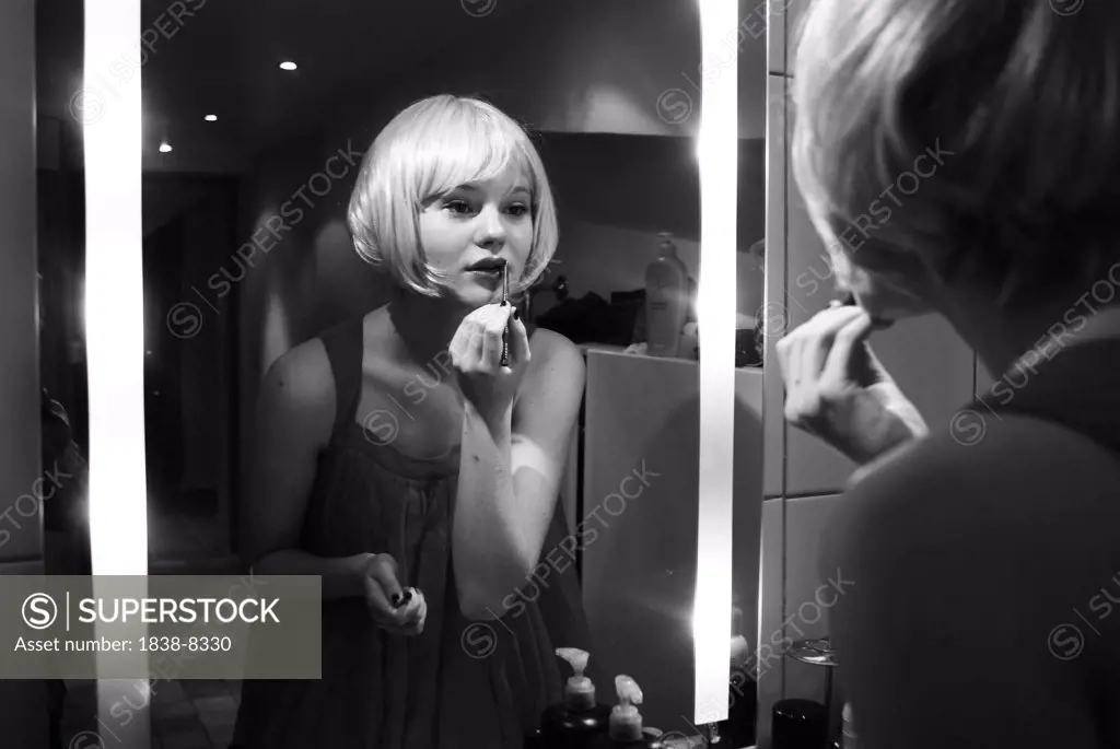 Young Blonde Woman Looking in Mirror and Applying Lip Gloss