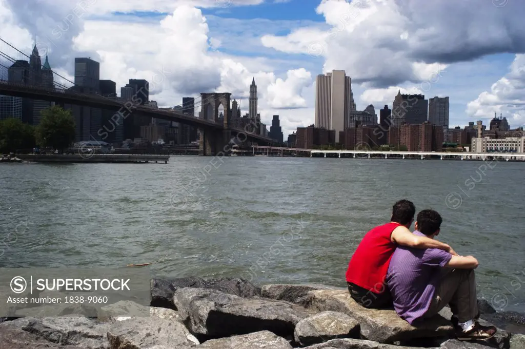 Two Men Sitting at Edge of River Looking at Lower Manhattan Skyline and Brooklyn Bridge, New York City, USA