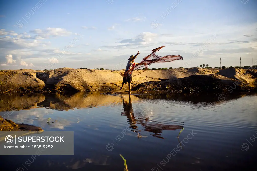 Young Man Tossing Fishing Net into Small Pond