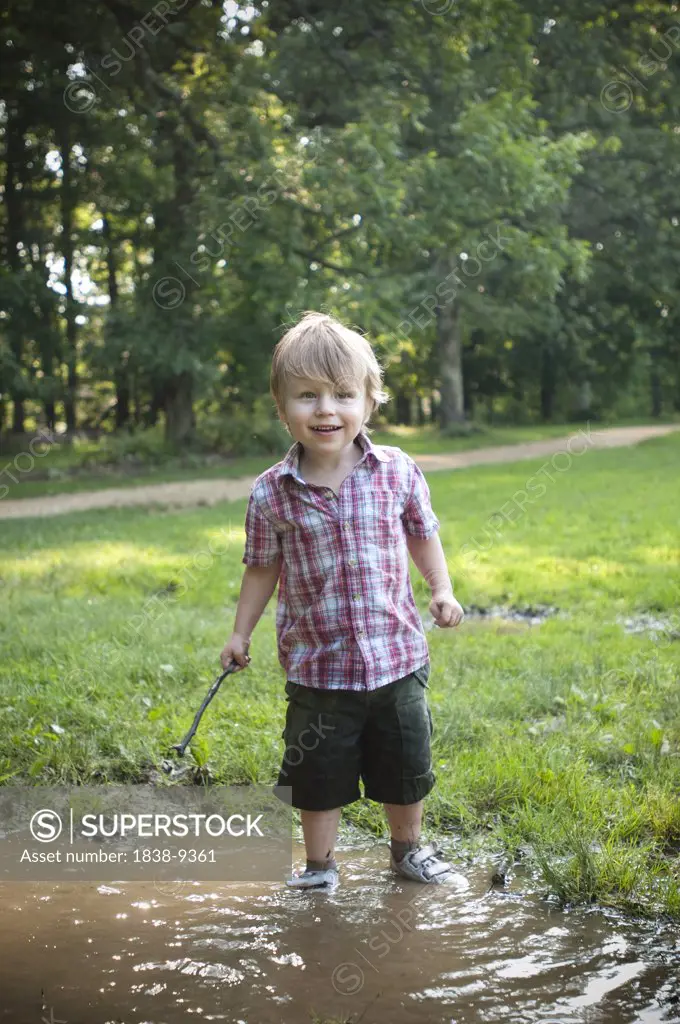 Smiling Young Boy Standing in Puddle and Holding Stick