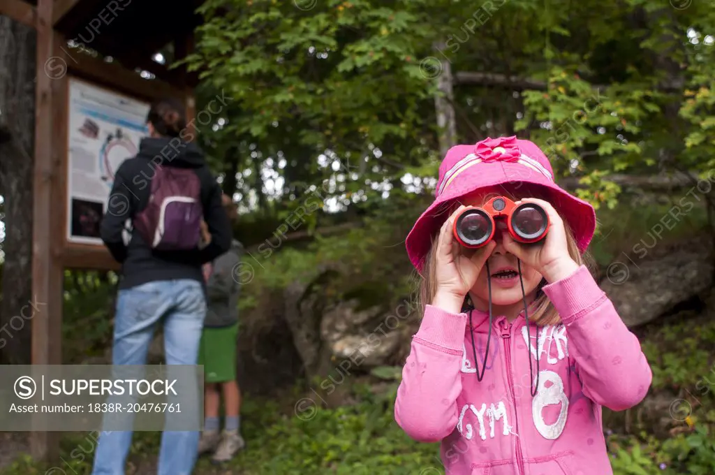 Young Girl Looking Through Binoculars While Woman and Young Boy Look at Hiking Map